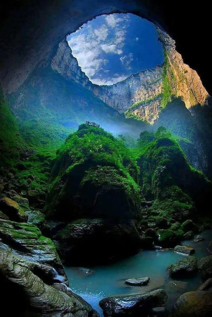 Interior de una cueva con paisaje surrealista, vegetación verde y cielo azul visto desde un entorno natural impresionante.
