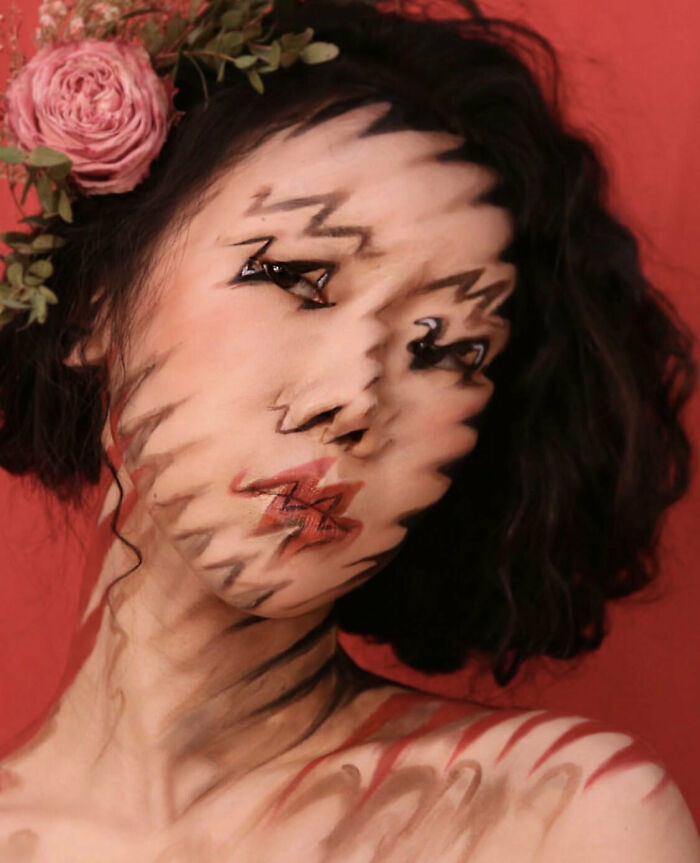 Rostro femenino con efecto surrealista y zigzags en piel, fondo rojo y flores rosas en el cabello.