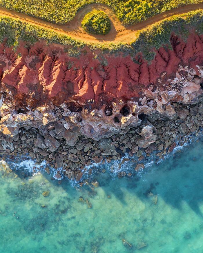 Vista aérea de costa con agua turquesa, rocas y tierra roja, creando imágenes sorprendentes con un toque de surrealismo.