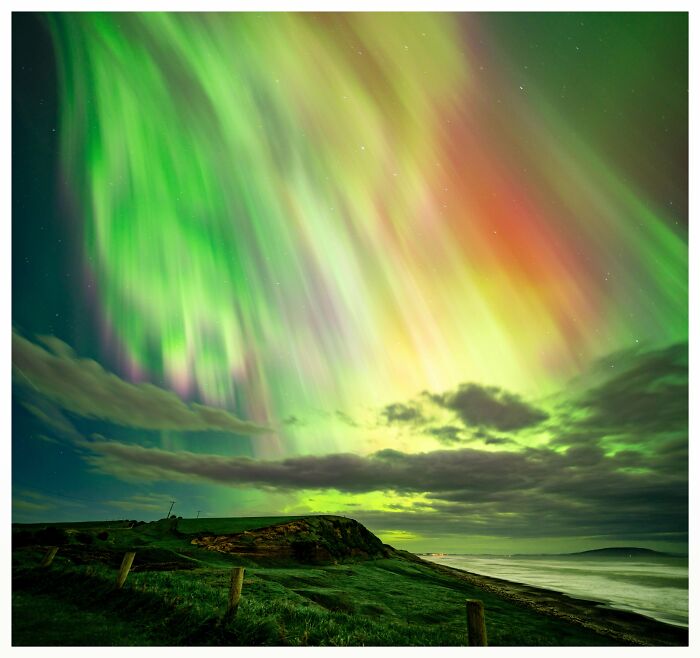 Aurora boreal sobre paisaje costero con un toque de surrealismo en colores verde y naranja brillantes.