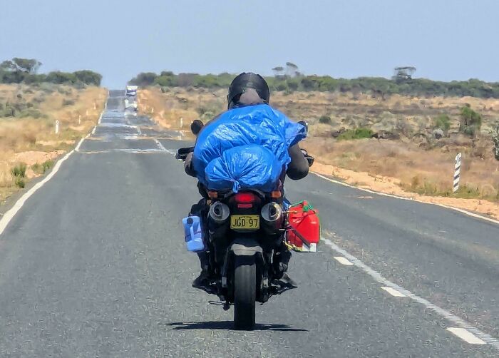 Persona viajando en motocicleta por una carretera solitaria en Australia, cargada con suministros.