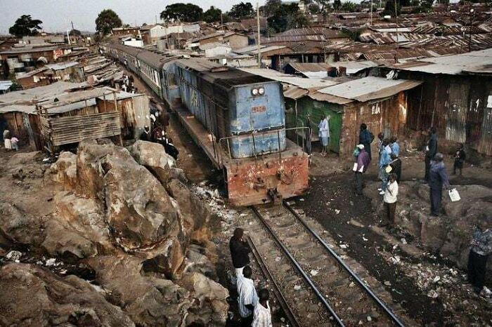 Tren pasando por una zona urbana abarrotada, reflejando el infierno urbano creado por la densidad y pobreza.