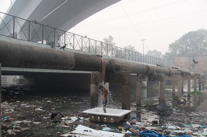 Persona usando una ducha improvisada bajo un puente, ejemplo del infierno urbano.
