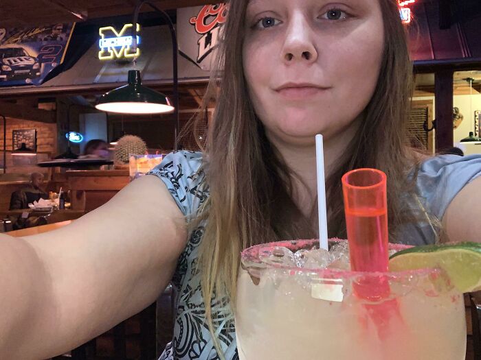 Mujer tomando selfie en bar con bebida, ilustrando citas que no salieron nada bien compartidas en internet.