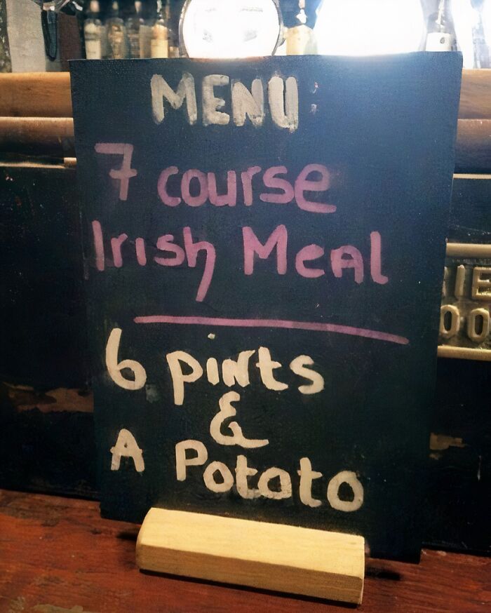 Pizarra con menú humorístico del Reino Unido que ofrece una comida irlandesa con seis pintas y una papa.