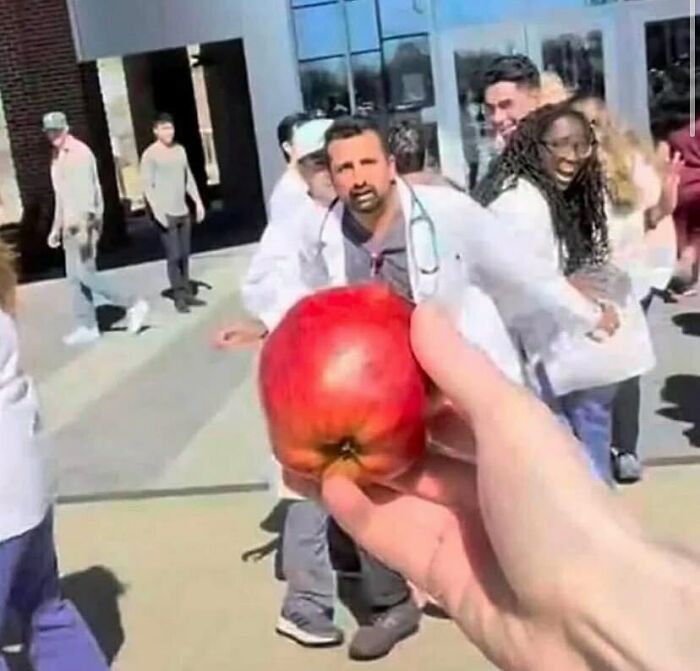 Mano sostiene manzana frente a grupo de personas riendo, imagen divertida que provoca risas y reacciones virales.