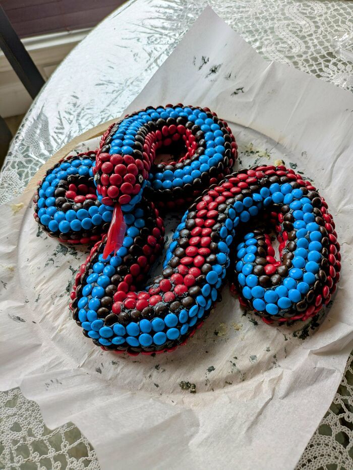 Tarta en forma de serpiente decorada con caramelos rojos, azules y negros mostrando creatividad en repostería nivel experto.
