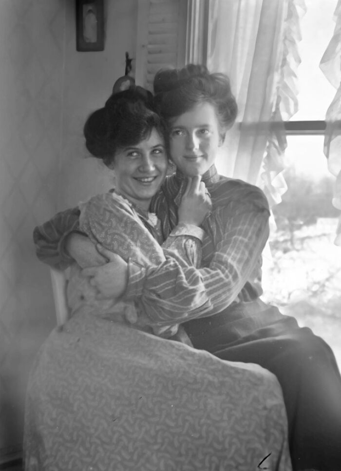 Dos mujeres abrazadas en interior con ropa típica de la época victoriana, mostrando tiempos muy distintos.