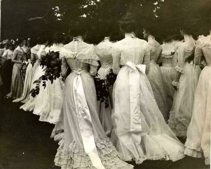 Mujeres con vestidos largos victorianos y lazos en la espalda en una ceremonia al aire libre, época victoriana.