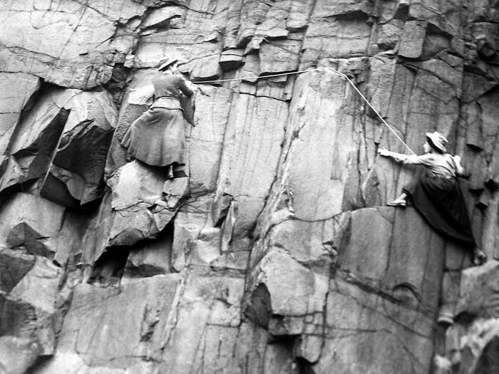 Dos mujeres de la época victoriana escalan una pared rocosa, mostrando la audacia y desafíos de ese tiempo.