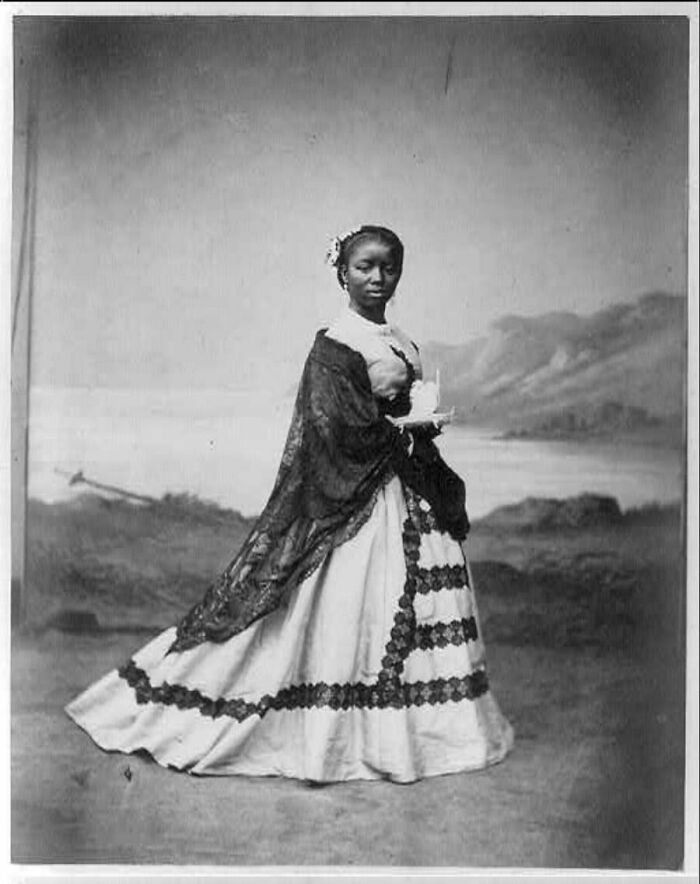 Mujer con vestido y mantón en imagen antigua de la época victoriana mostrando moda y estilo distintivo.