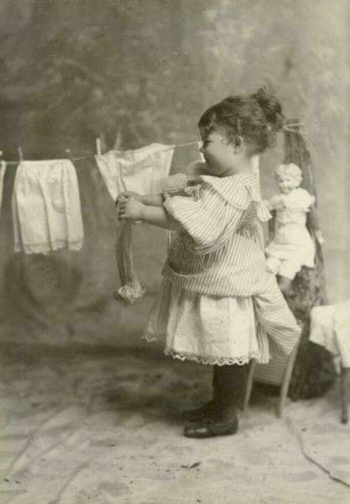 Niña victoriana colgando ropa pequeña en un tendedero en una imagen antigua de la época victoriana.