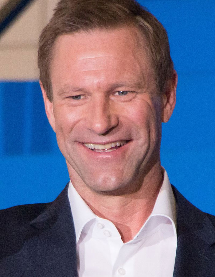 Hombre sonriente con traje oscuro en evento, representación de celebridades que se desvanecieron en el tiempo.