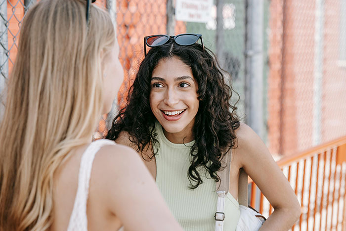 Dos mujeres conversando animadamente al aire libre, compartiendo códigos de trucos para el juego de la vida.