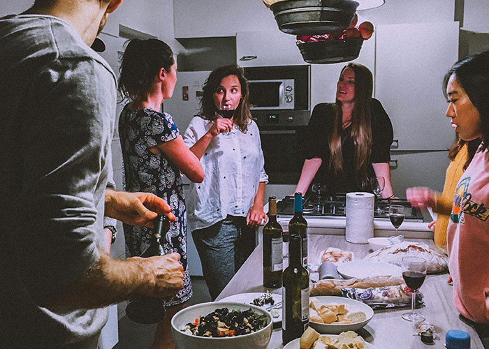 Personas reunidas en cocina compartiendo vino y comida, simbolizando códigos de trucos para el juego de la vida.