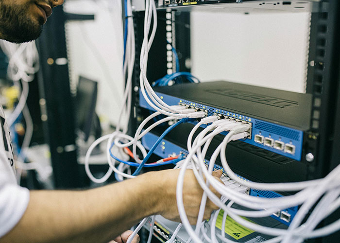 Persona conectando cables en un panel de red, mostrando códigos de trucos para el juego de la vida en entorno tecnológico.