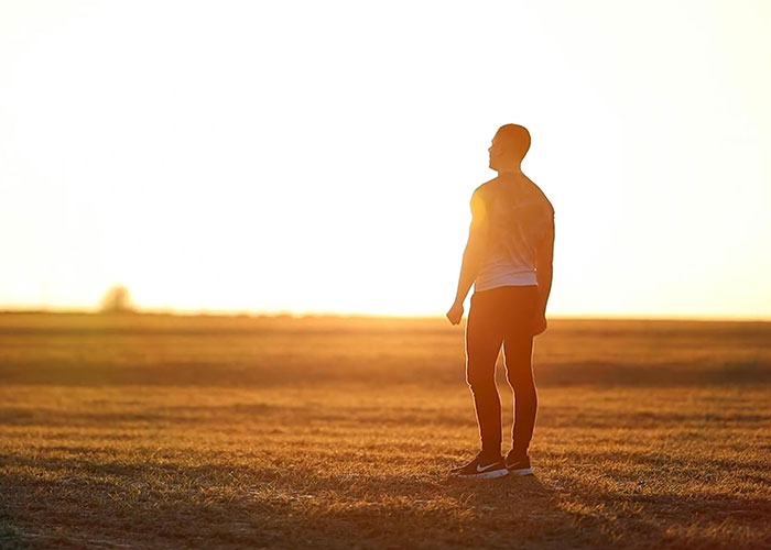 Hombre de pie al atardecer en campo abierto, simbolizando códigos de trucos para el juego de la vida.