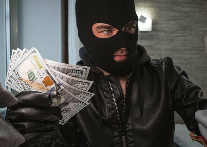 Persona enmascarada con chaqueta de cuero sosteniendo billetes, evocando secretos familiares de terror.