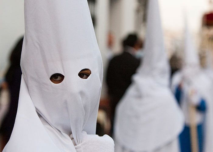 Persona en túnica y capucha blanca durante una procesión, evocando secretos familiares inquietantes.