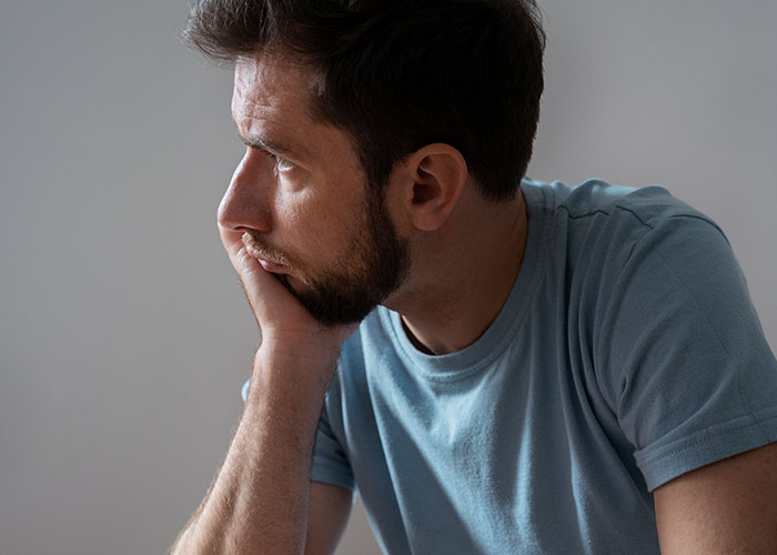 Hombre pensativo con camiseta azul clara, reflejando secretos familiares inquietantes.