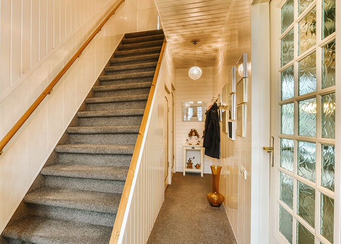 Pasillo hogareño con escalera y decoración sencilla, evocando secretos familiares misteriosos.