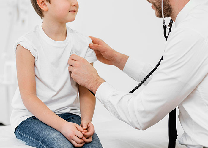 Niño en consulta médica, doctor revisando con estetoscopio, posible escena de secretos familiares.