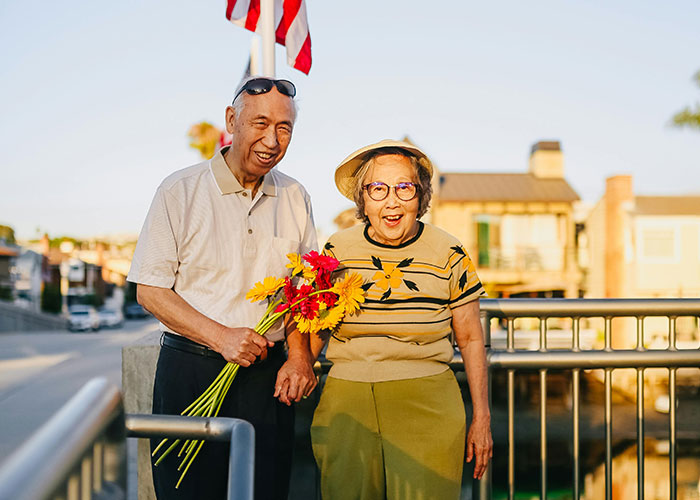 Pareja sonriente al aire libre con flores bajo luz de tarde, casas de fondo.