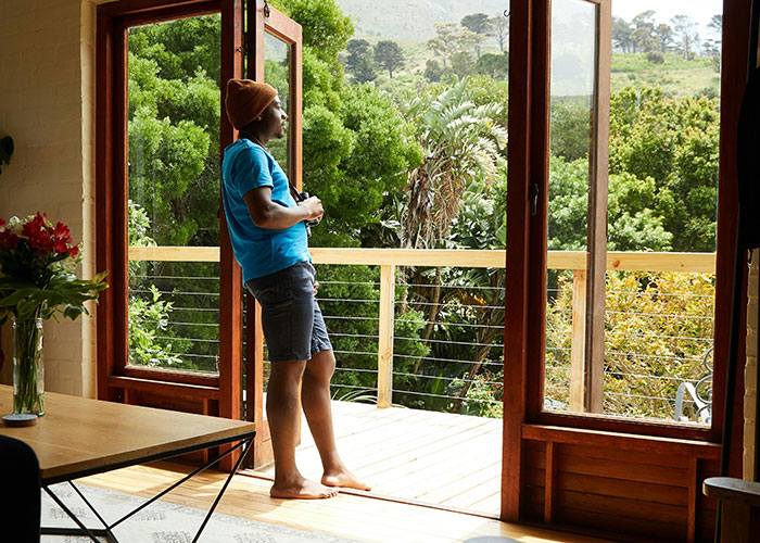 Hombre de pie en casa moderna con vista natural, relajado y reflexionando sobre códigos de trucos para el juego de la vida.