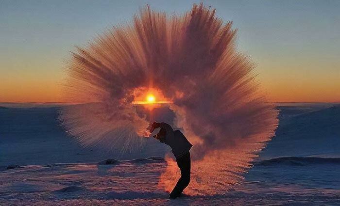 Persona lanzando agua congelada al aire al atardecer creando efecto de surrealismo en paisaje nevado.