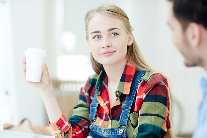 Joven sonriente sosteniendo vaso mientras conversa con otra persona demostrando estupideces dichas con seriedad.