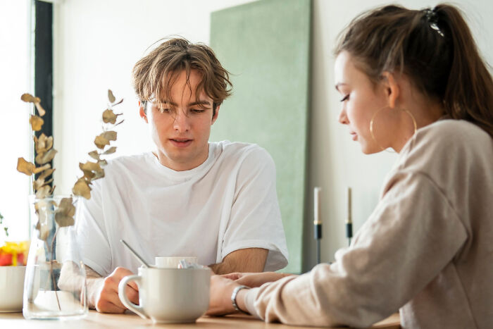 Jóvenes conversando seriamente en una mesa con tazas, mostrando expresiones que reflejan estupideces dichas en serio.