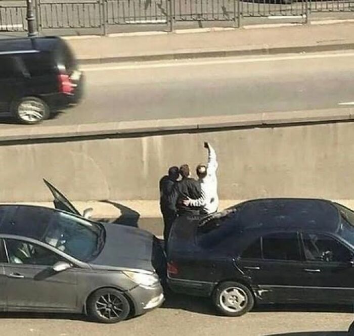 Tres personas en la carretera toman un selfie tras un accidente de coches, escena rara y sorprendente.