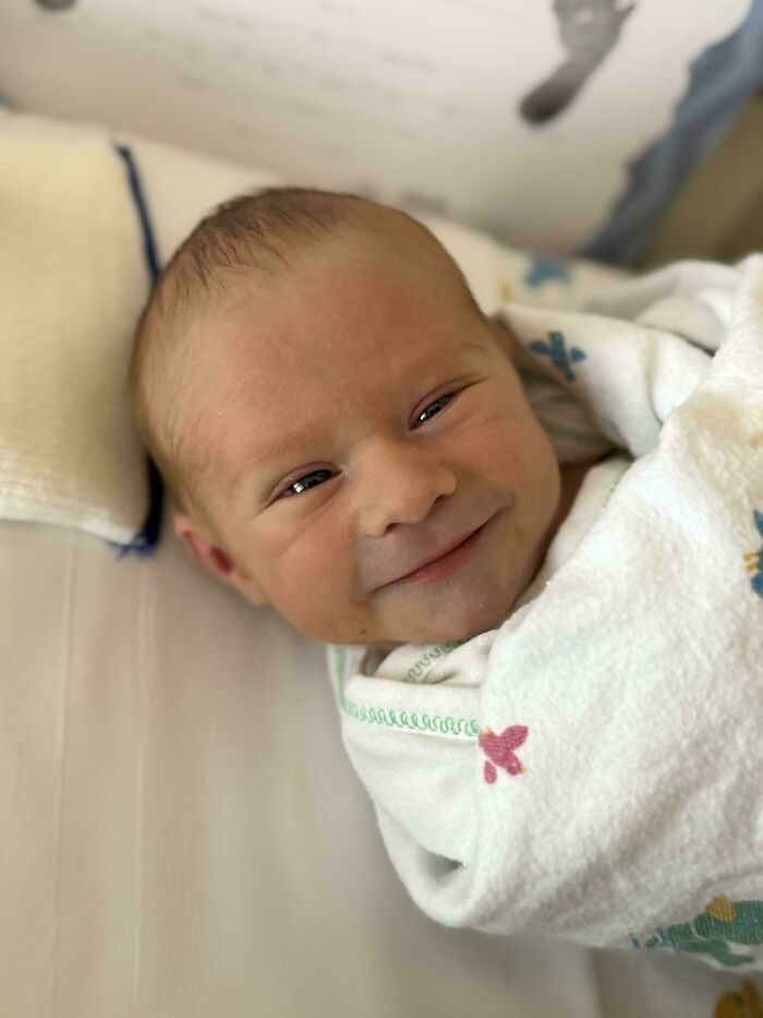Bebé recién nacido sonriendo envuelto en manta, momento entrañable y divertido de paternidad con fotos preciosas de padres.