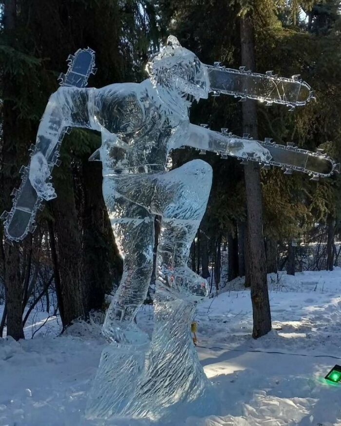 Escultura de hielo de figura humana con motosierras en bosque nevado, imagen que provoca risas y asombro.
