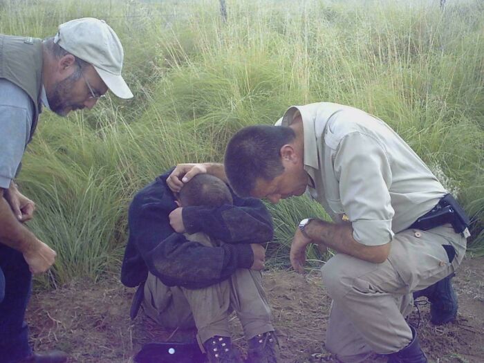 Un niño en el suelo abrazado por dos hombres en un suceso increíble en un campo.