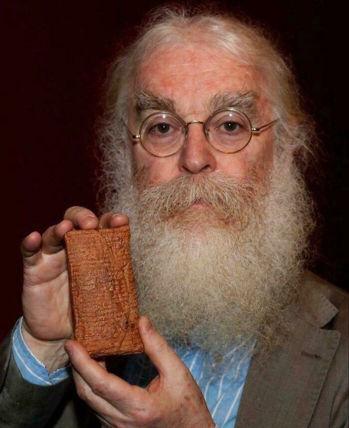 Hombre mayor con gafas y barba larga sosteniendo una tablilla antigua, representando un momento increíble.