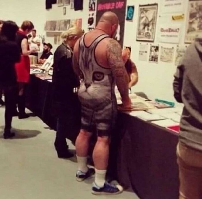 Hombre musculoso con tatuajes, vestido con un traje de gato divertido, en una feria o exposición concurrida.