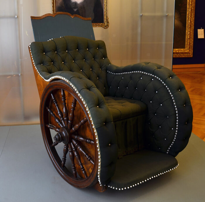 Silla de ruedas antigua con diseño acolchado, muestra del pasado lejano en exhibición.
