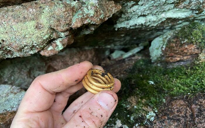 Persona sosteniendo un hallazgo fascinante que ofrece un vistazo al pasado lejano, frente a fondo rocoso y musgoso.