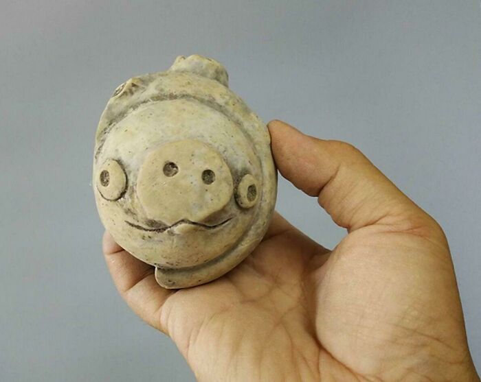 Mano sosteniendo artefacto antiguo con forma de cara, permitiendo un vistazo al pasado lejano.