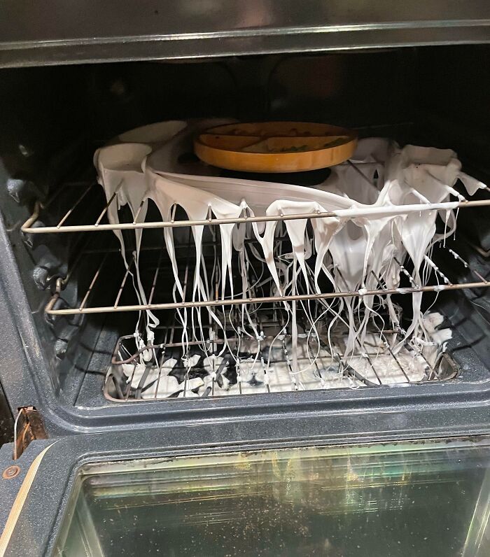 Horno con desastre causado por hombres, masa blanca desbordada en las rejillas y plato en la parte superior.