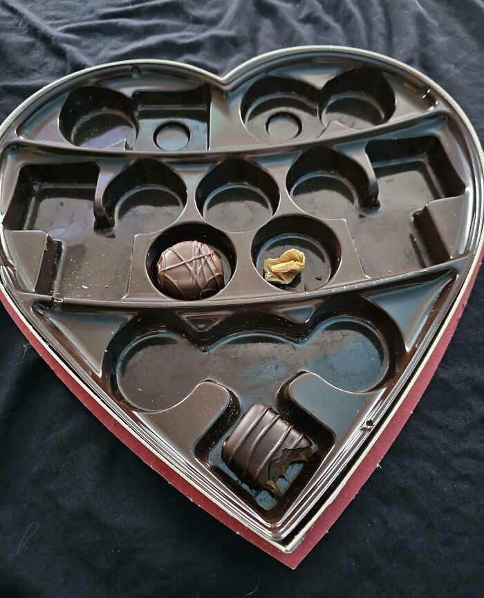 Caja de chocolates en forma de corazón con solo dos chocolates restantes y un envoltorio vacío.
