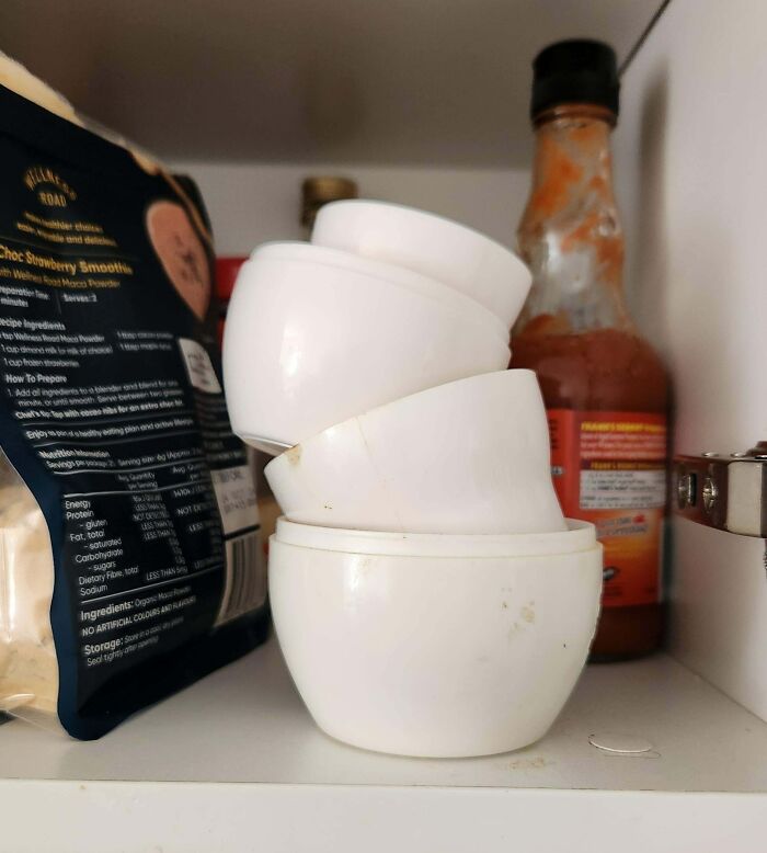 Tazones de plástico apilados desordenadamente en un estante con salsa picante al fondo.