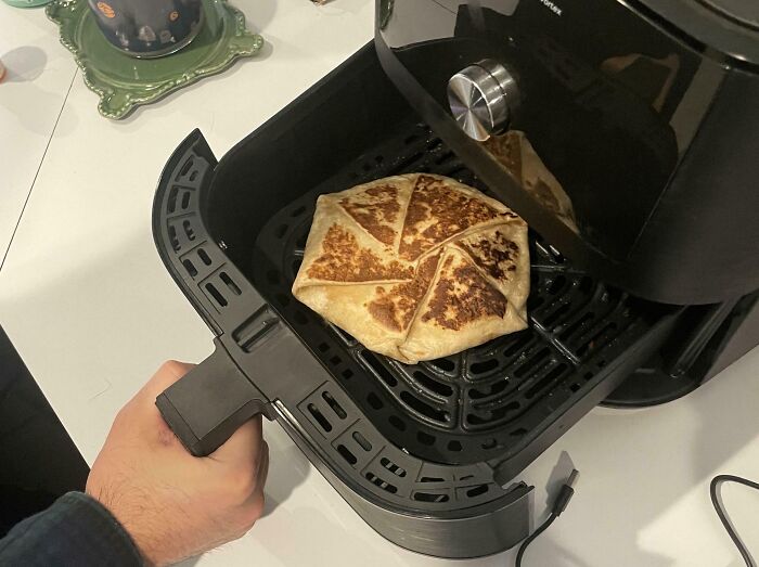Hombre cocinando un burrito en una freidora de aire negra.