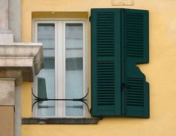 Persiana verde mal ajustada deja parte de la ventana descubierta, mostrando un fallo de arquitectura simpático.
