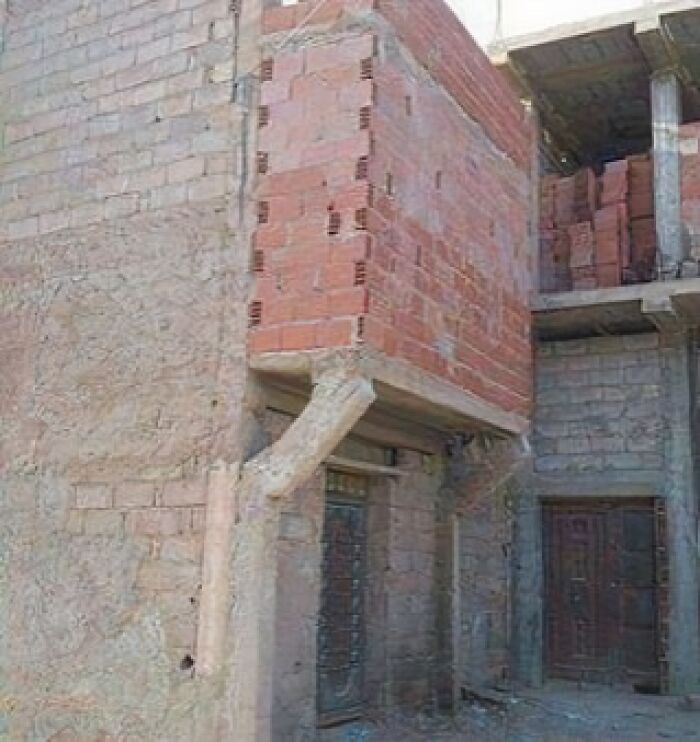 Construcción con fallos de arquitectura, paredes de ladrillo rojo mal colocadas y columnas inestables.