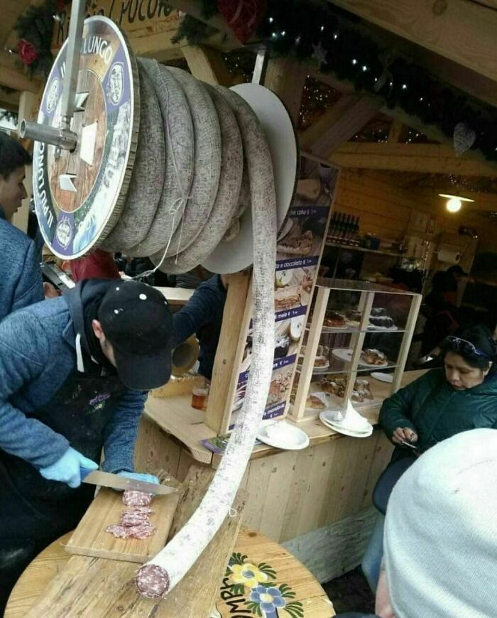 Persona cortando embutido largo enrollado en carretel en mercado, una de las cosas que sorprendieron a los viajeros.