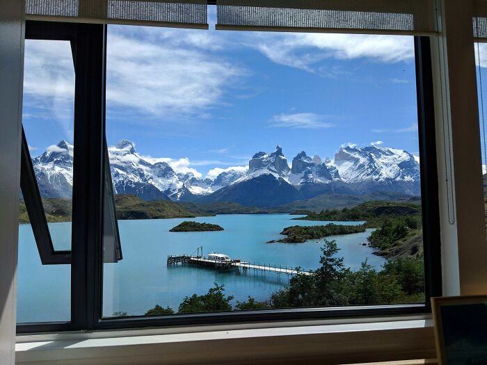 Vista desde una ventana de montañas nevadas y lago azul con muelle, sorprendiéndose viajeros en otros países.