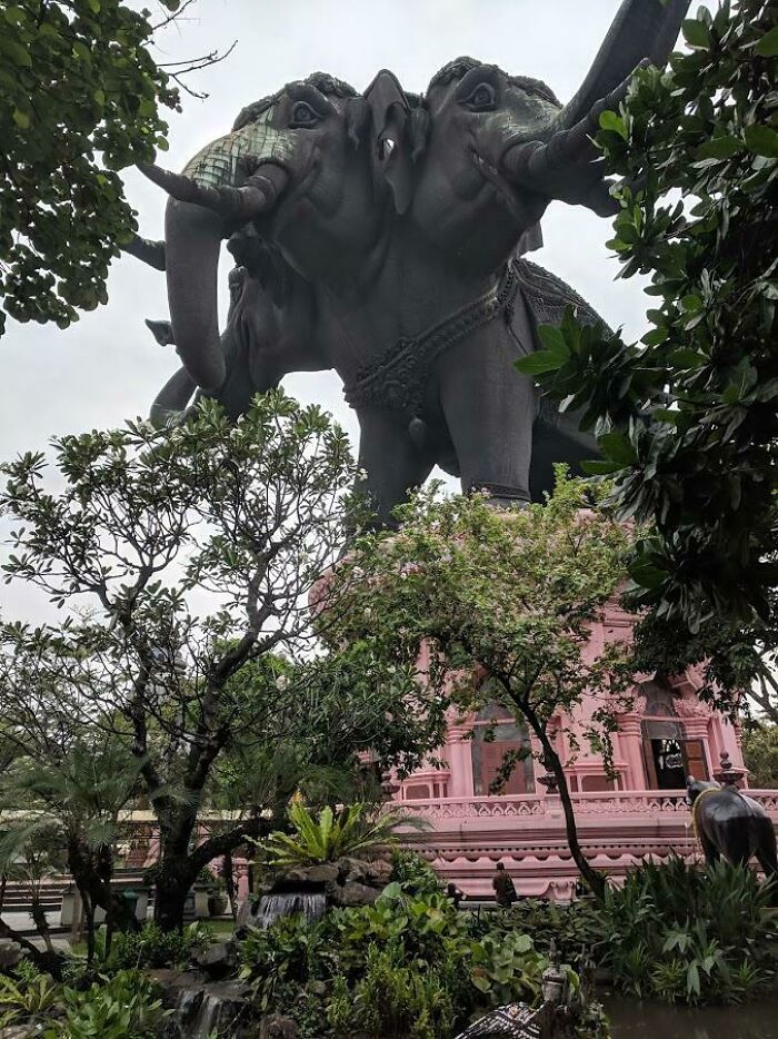 Escultura de elefantes de tres cabezas en un templo rodeado de vegetación, sorprendente para viajeros en otros países.