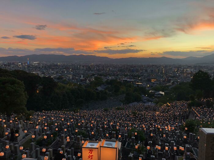 Atardecer sobre cementerio iluminado con miles de luces en paisaje urbano, sorprendiendo a los viajeros en otros países.